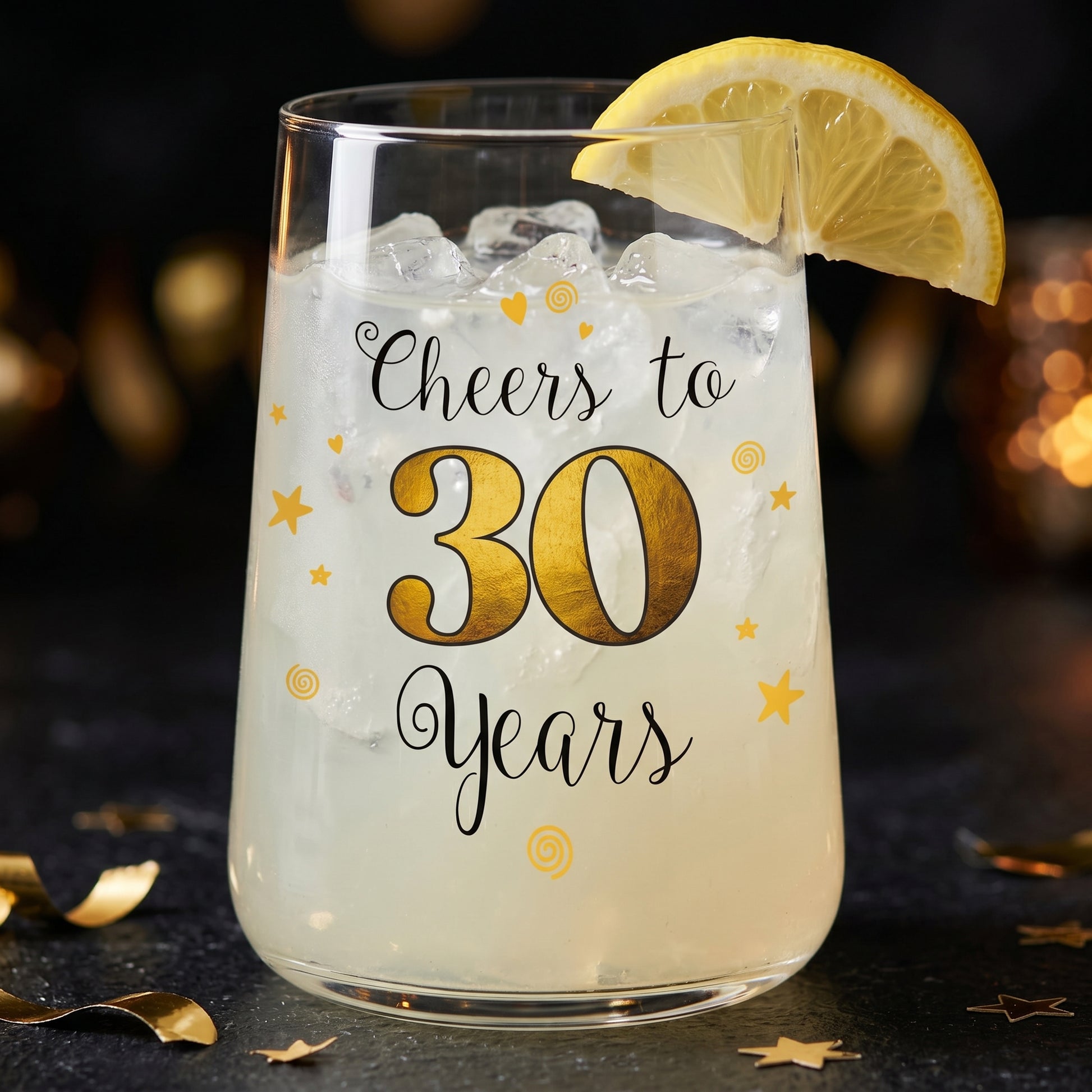 Trinkglas mit Cheers to 30 Years Aufdruck, Zitronenscheibe und hellem Drink auf dunklem Partytisch