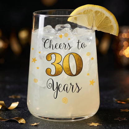 Trinkglas mit Cheers to 30 Years Aufdruck, Zitronenscheibe und hellem Drink auf dunklem Partytisch