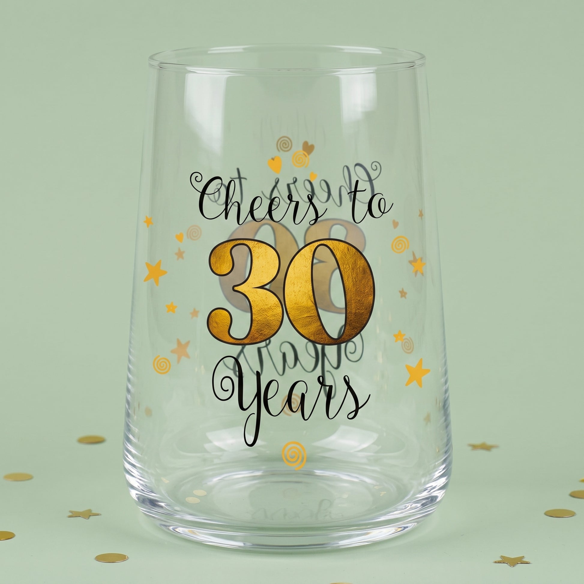 Leeres Trinkglas mit Cheers to 30 Years Aufdruck, goldener 30 und Sternen auf grünem Hintergrund