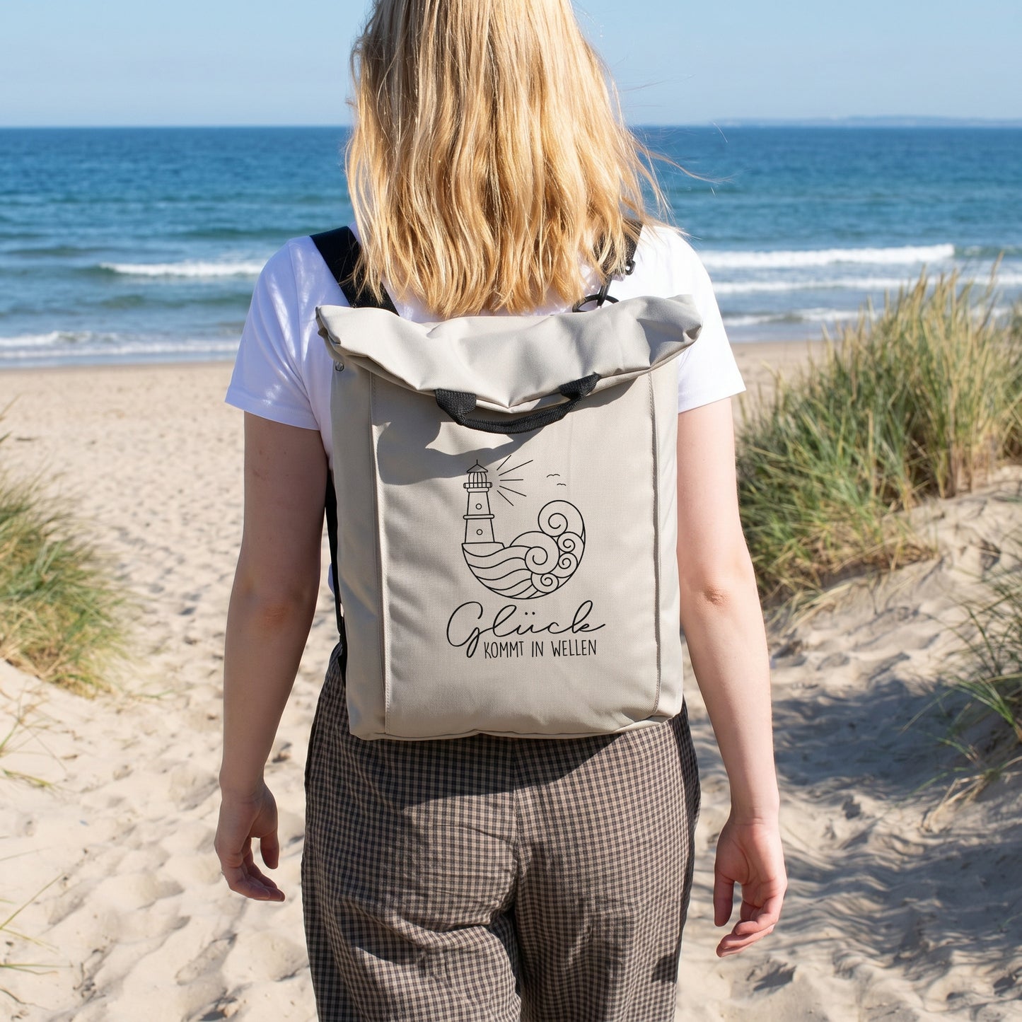Beiger Rucksack mit Leuchtturm Motiv wird am Strand getragen und eignet sich für Urlaub, Wandern und Freizeit