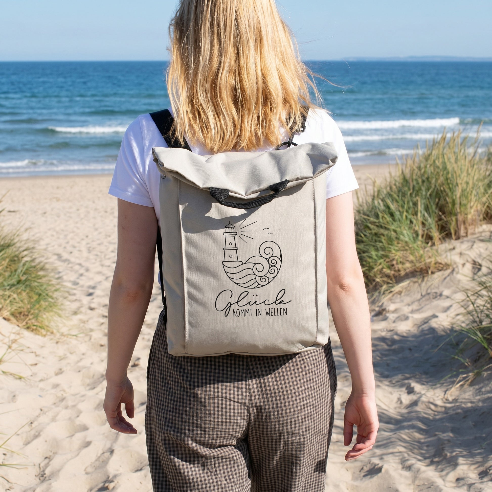 Beiger Rucksack mit Leuchtturm Motiv wird am Strand getragen und eignet sich für Urlaub, Wandern und Freizeit