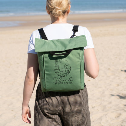 Jadegrüner 2-in-1 Rucksack mit Spruch Glück kommt in Wellen auf dem Rücken am Strand getragen