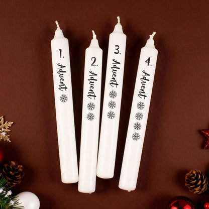 Adventskerzen-Set mit vier weißen Stabkerzen, beschriftet mit 1. bis 4. Advent und Schneeflocken, auf braunem Hintergrund.