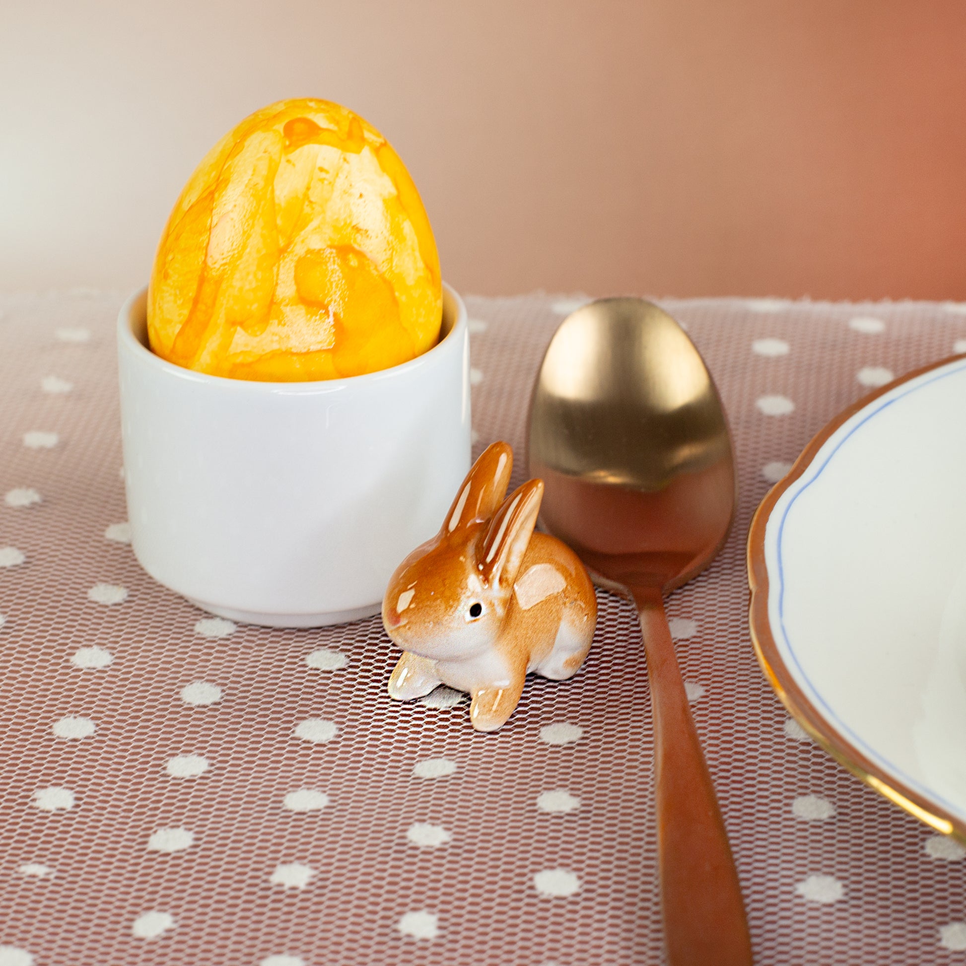 Keramik-Häschen als Tischdeko zu Ostern neben Osterei und Besteck