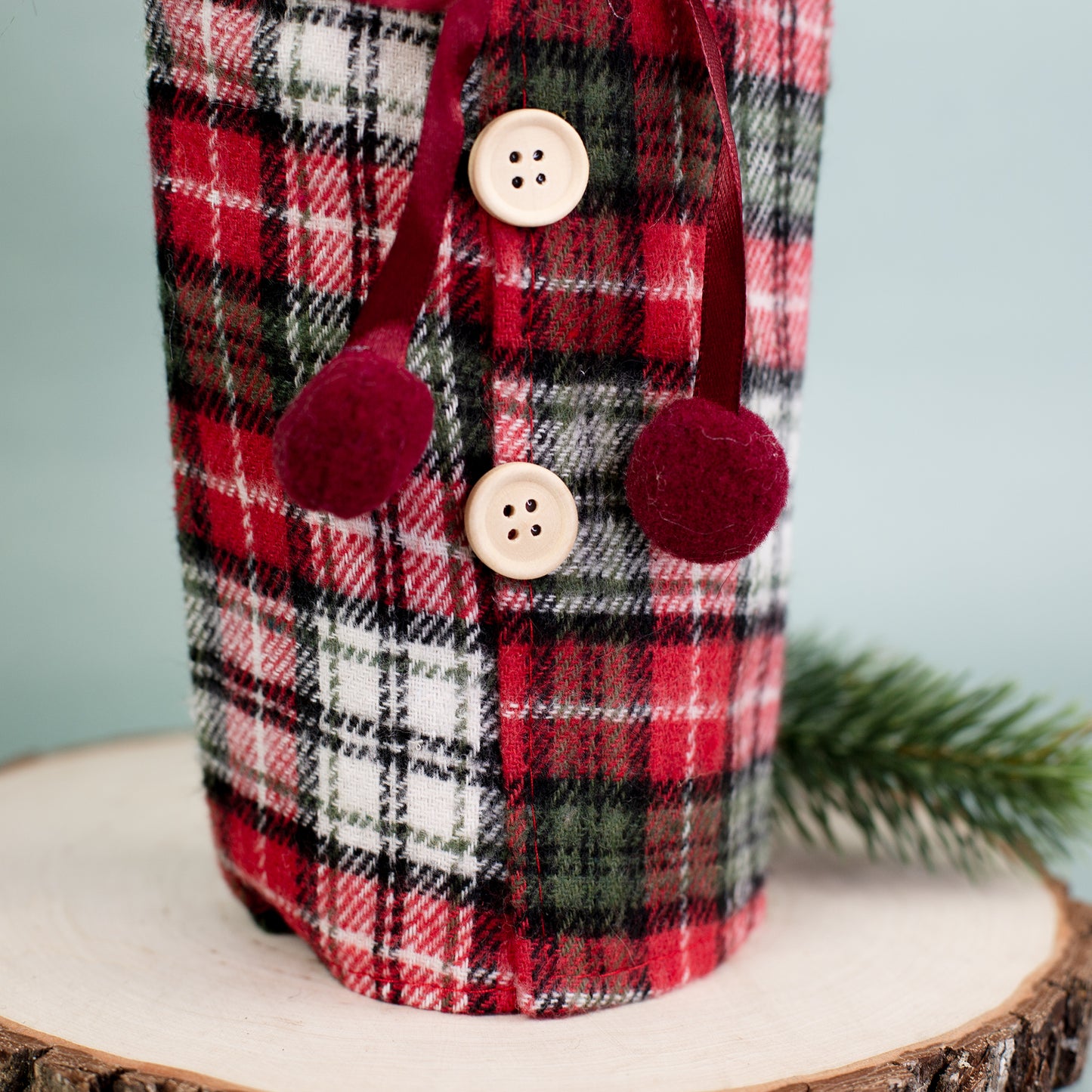 Detailaufnahme der Knopfleiste der karierten Flaschenverpackung mit roten Bommeln und Holzknöpfen.