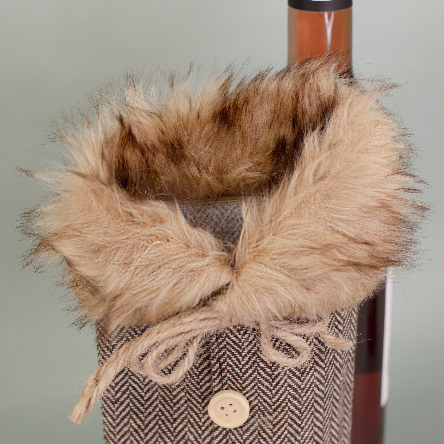Nahaufnahme des Pelzkragens der braunen Flaschen Geschenkverpackung in Mantel-Optik mit Kordel und Knöpfen.