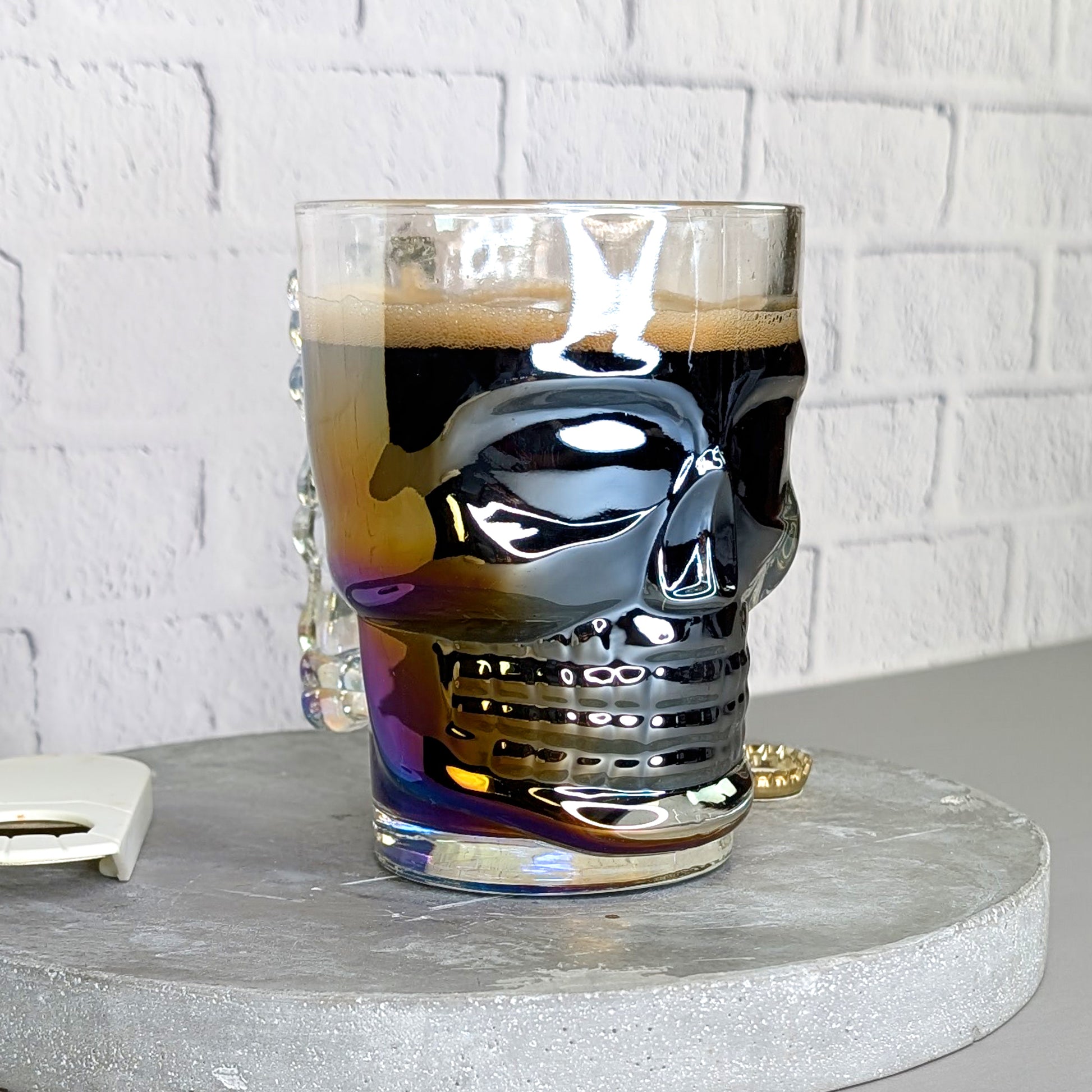 Totenkopfglas leicht schräg von vorne gefüllt mit dunklem Bier und irisierendem Effekt