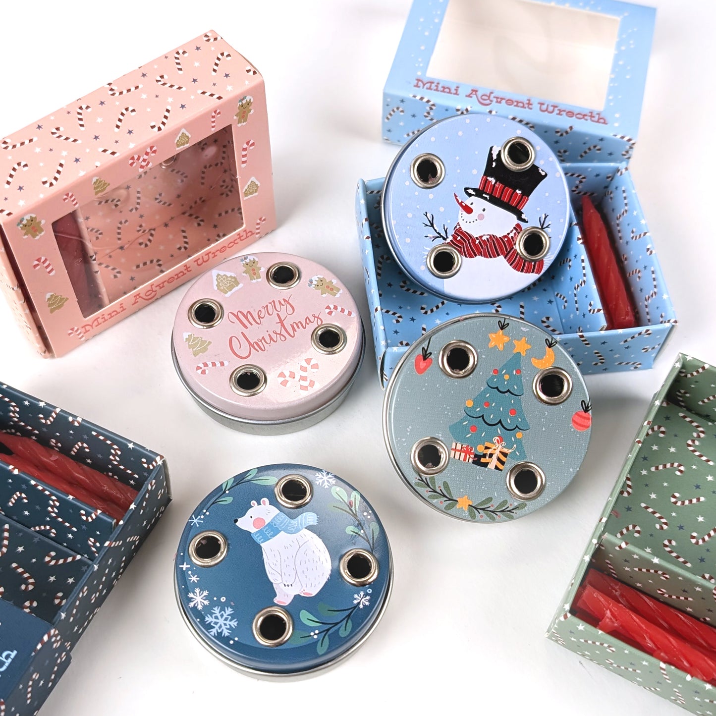 Vier verschiedene Mini-Adventskränze mit Motiven „Schneemann“, „Weihnachtsbaum“, „Eisbär“ und „Merry Christmas“, jeweils mit passenden Geschenkverpackungen und roten Mini-Kerzen, auf weißem Hintergrund.