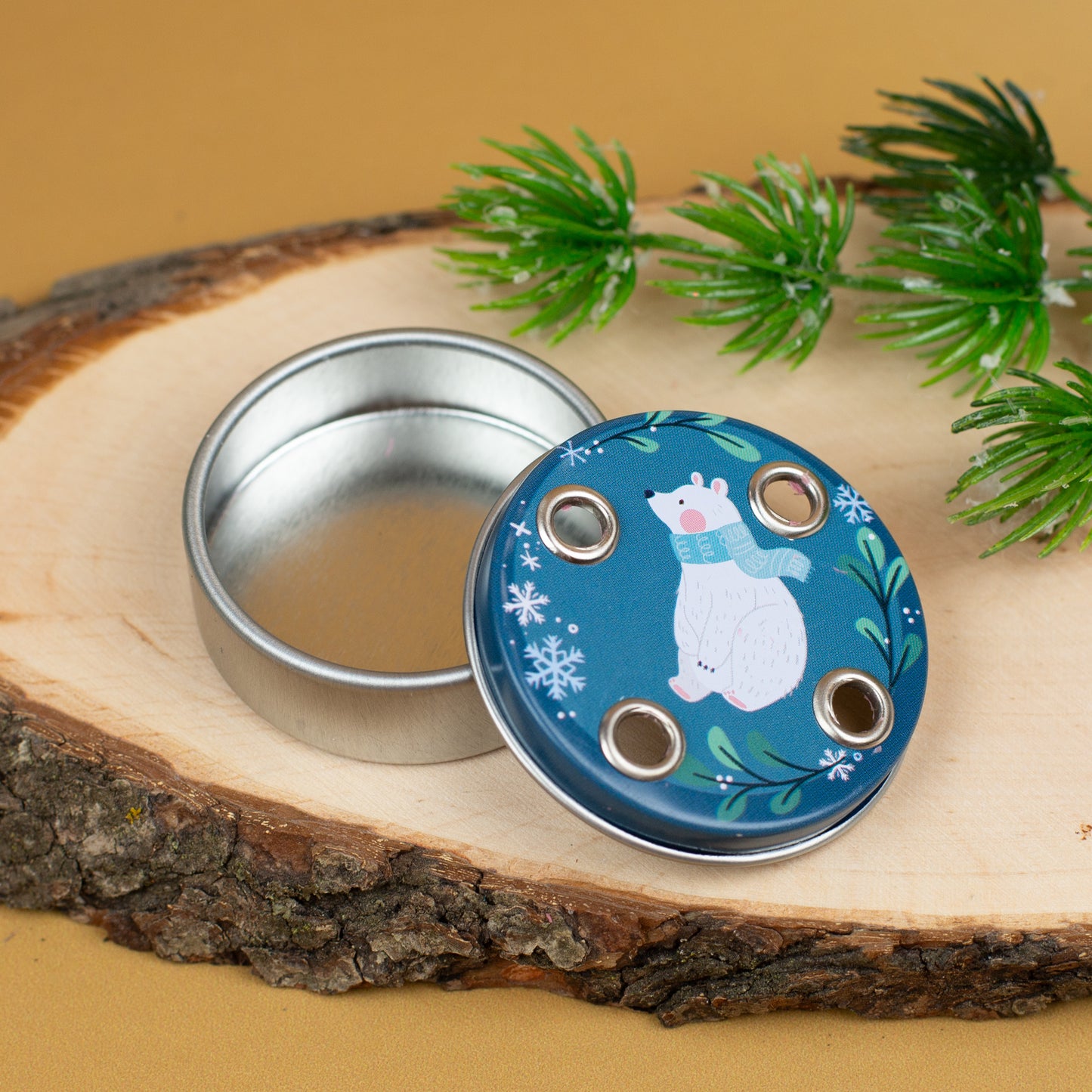 Geöffnete Metalldose mit vier Kerzenhalterungen im Deckel, dekoriert mit einem weißen Eisbären und Schneeflockenmotiv, platziert auf einem Holzstück mit künstlichem Tannenzweig.