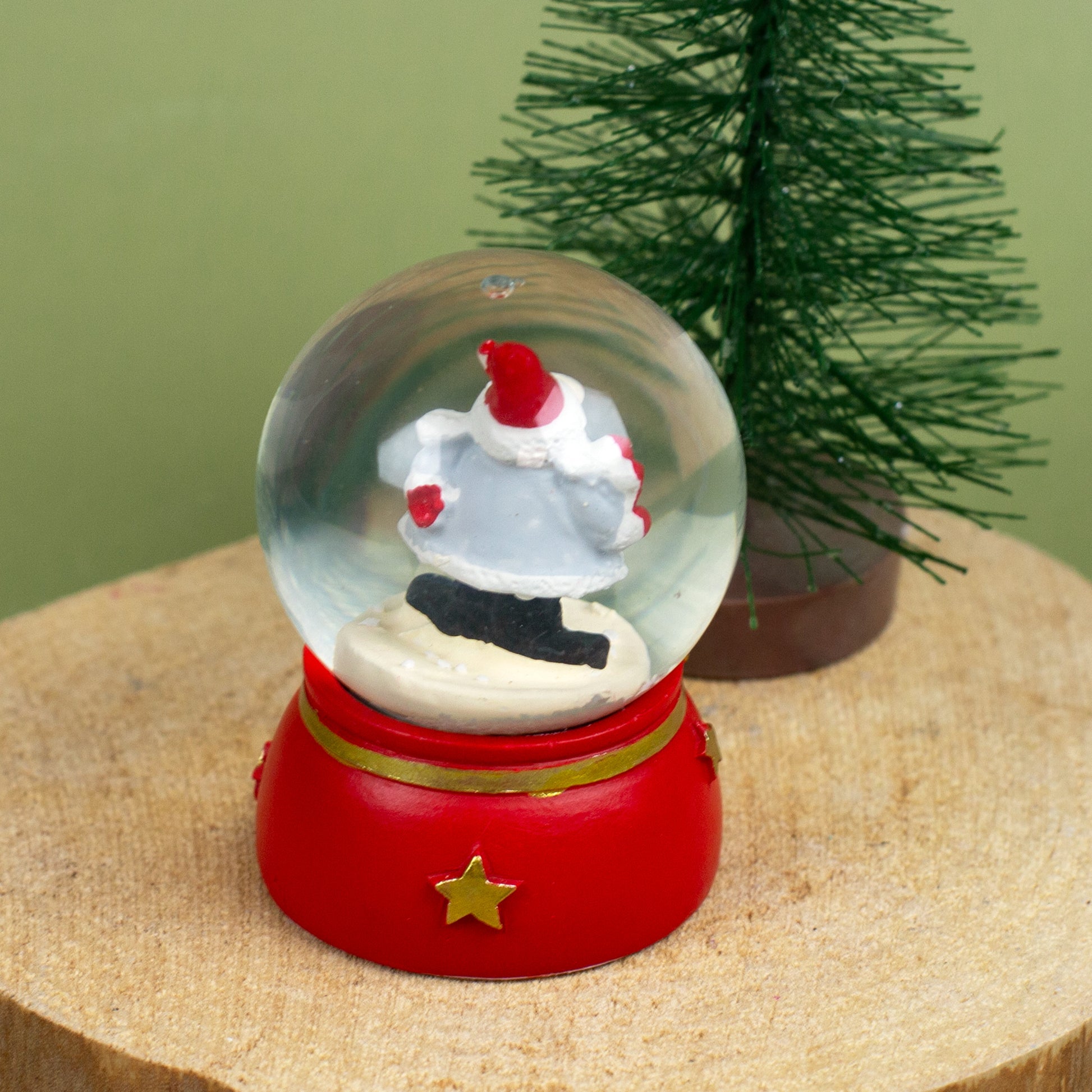 Schneekugel mit Weihnachtswichtel, der ein rotes Herz in den Händen hält, auf Holzuntergrund dekoriert