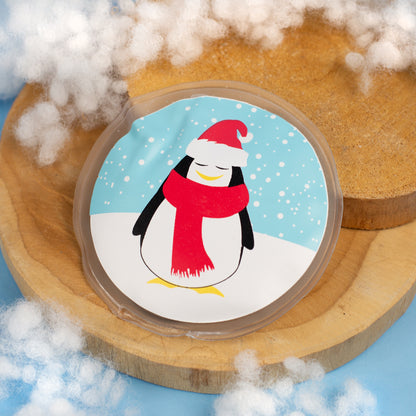 Runder Handwärmer mit Pinguinmotiv auf Holzunterlage und Kunstschnee