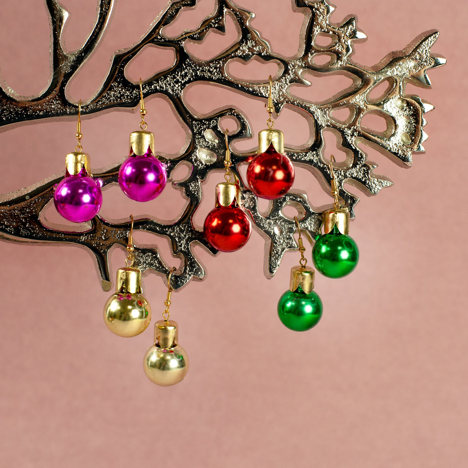 Vier Paar Weihnachtskugel-Ohrringe in Pink, Gold, Rot und Grün hängend an silbernem Dekobaum