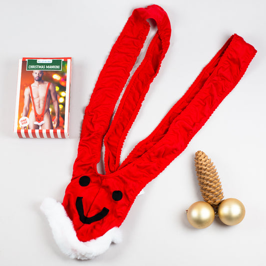 Roter Weihnachts-Mankini flach auf hellem Hintergrund, Verpackung daneben.