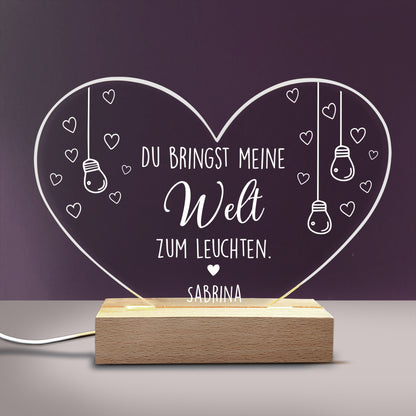 Personalisierte Acryl-LED-Lampe in Herzform mit Spruch „Du bringst meine Welt zum Leuchten“ und Name „Sabrina“ auf Holzsockel