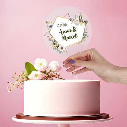 Personalisierter Tortentopper Hochzeit aus Acryl mit Namen Anna & Marcel und Datum auf weißer Torte vor rosa Hintergrund