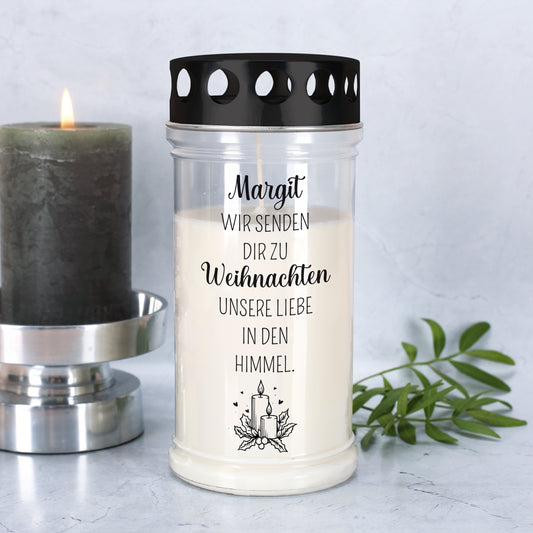 Erinnerungs-Grablicht mit Name „Margit“ und Weihnachtsmotiv, daneben brennende Kerze und grüner Zweig
