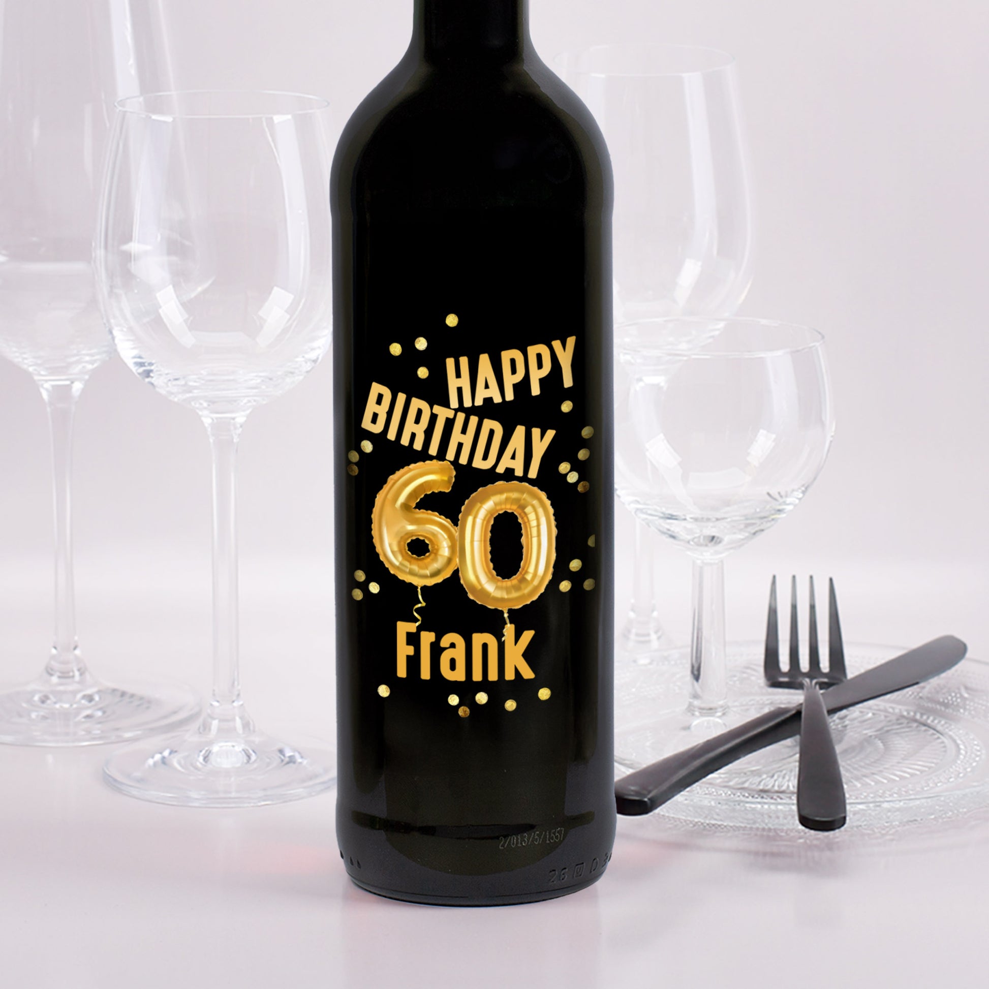 Weinflasche mit schwarzem Etikett zum 60. Geburtstag, goldene Ballons „60“, Name Frank, Hintergrund mit Besteck und Weingläsern
