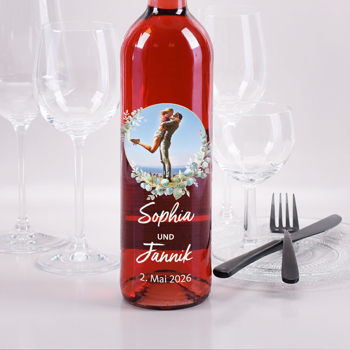 Personalisierte Roséweinflasche mit Foto im Eukalyptuskranz, Namen „Sophia und Jannik“ und Hochzeitsdatum.