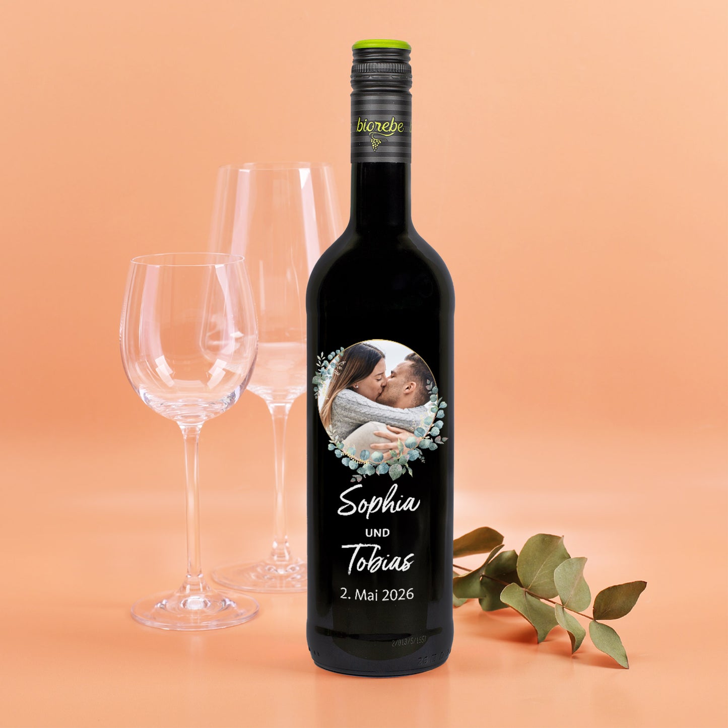 Personalisierte Rotweinflasche mit Foto und Eukalyptuskranz, Namen „Sophia und Tobias“ und Hochzeitsdatum.