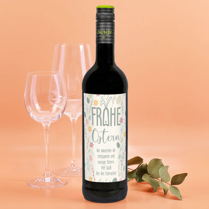 Rotweinflasche mit Osteretikett „Frohe Ostern“, vor orangem Hintergrund mit Gläsern