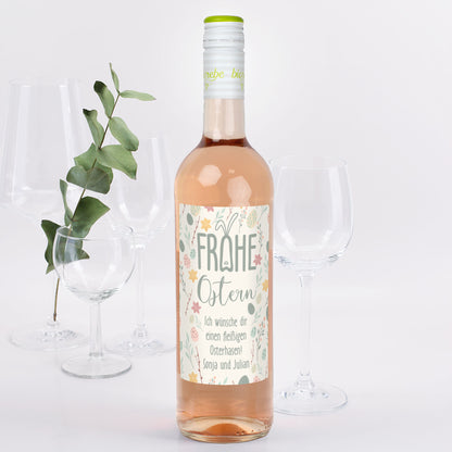 Weinflasche Rosé mit Osteretikett „Frohe Ostern“, daneben Gläser und Deko