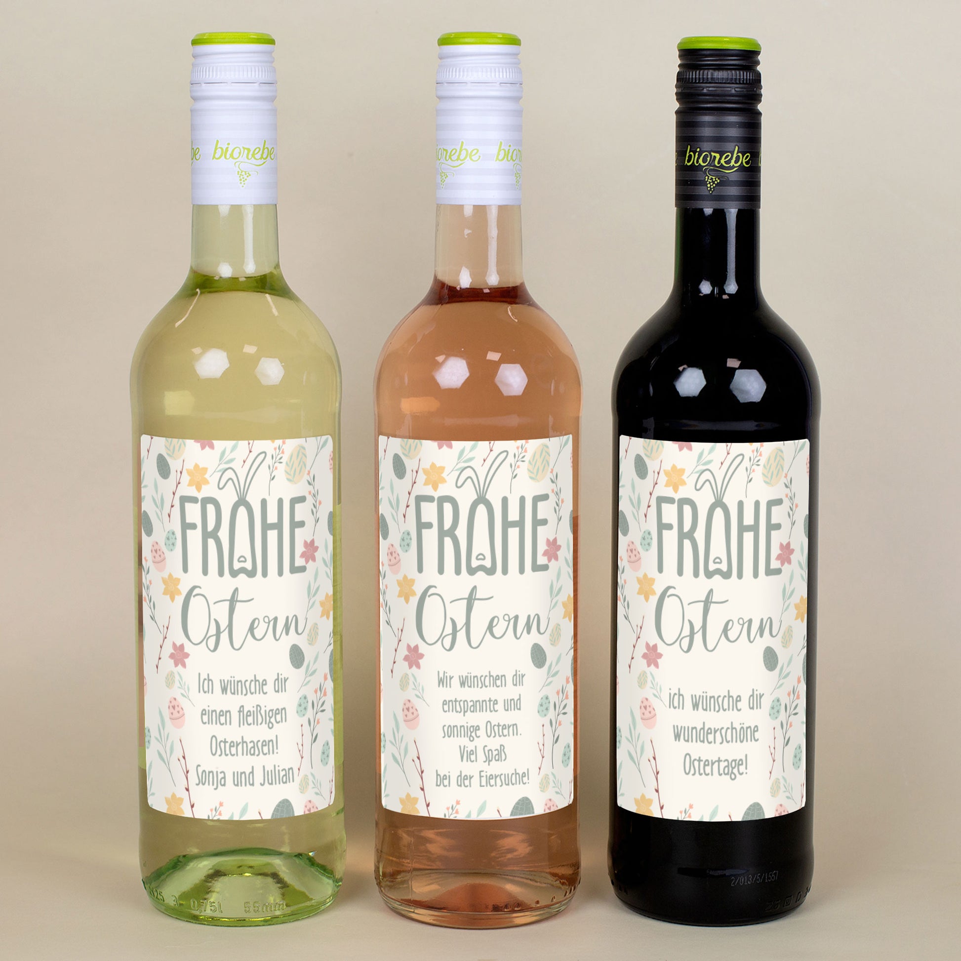 Drei Weinflaschen (Weißwein, Rosé, Rotwein) mit Osteretiketten „Frohe Ostern“ nebeneinander
