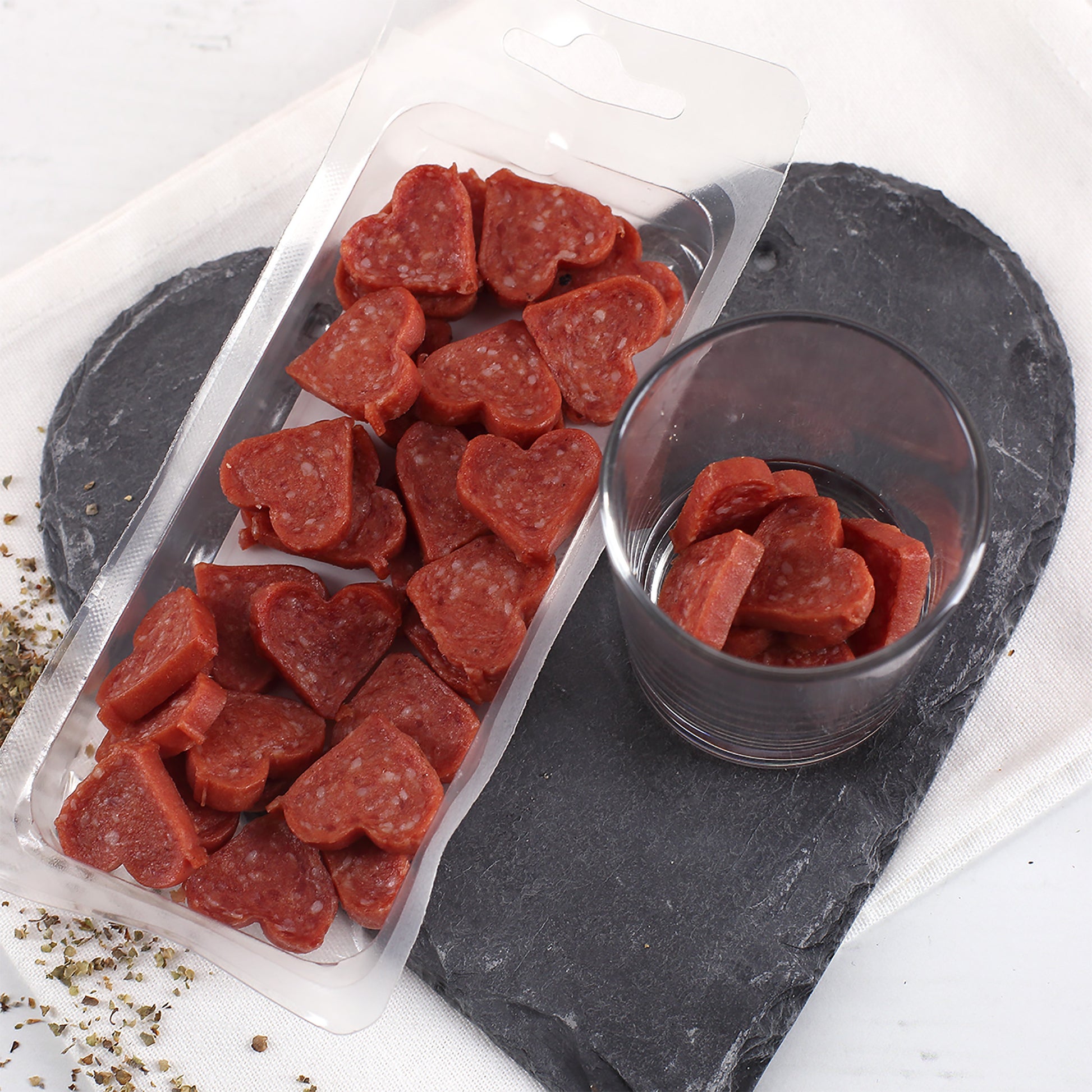 Geöffnete Verpackung mit Salami Herzen und Glas als herzhafter Snack für Männer