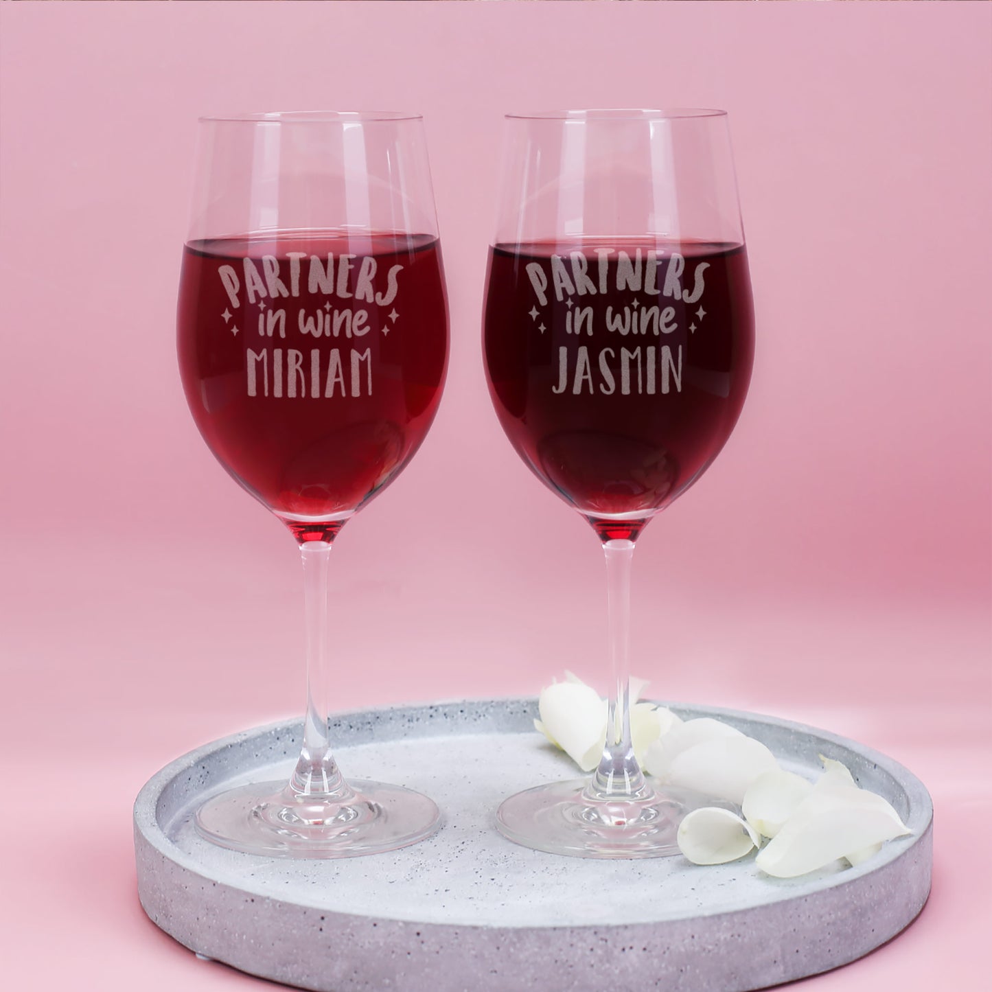 Zwei gravierte Weingläser mit der Aufschrift „Partners in Wine“ und den Namen Miriam und Jasmin, gefüllt mit Rotwein