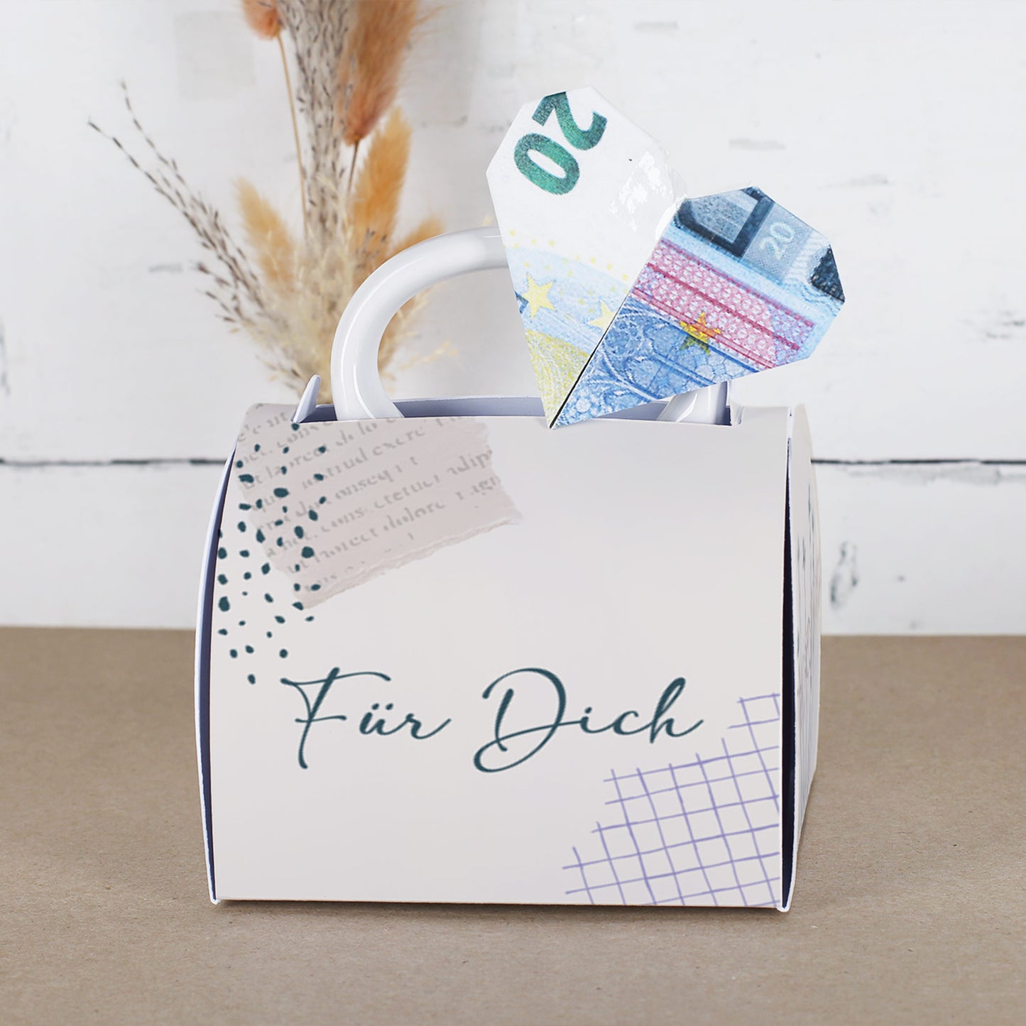 Fototasse in Geschenkverpackung mit „Für Dich“-Aufschrift, aus der ein Herz aus einem gefalteten 20-Euro-Schein ragt. Die Verpackung hat ein dezentes, modernes Design mit grafischen Elementen und wirkt wie eine kleine Handtasche.
