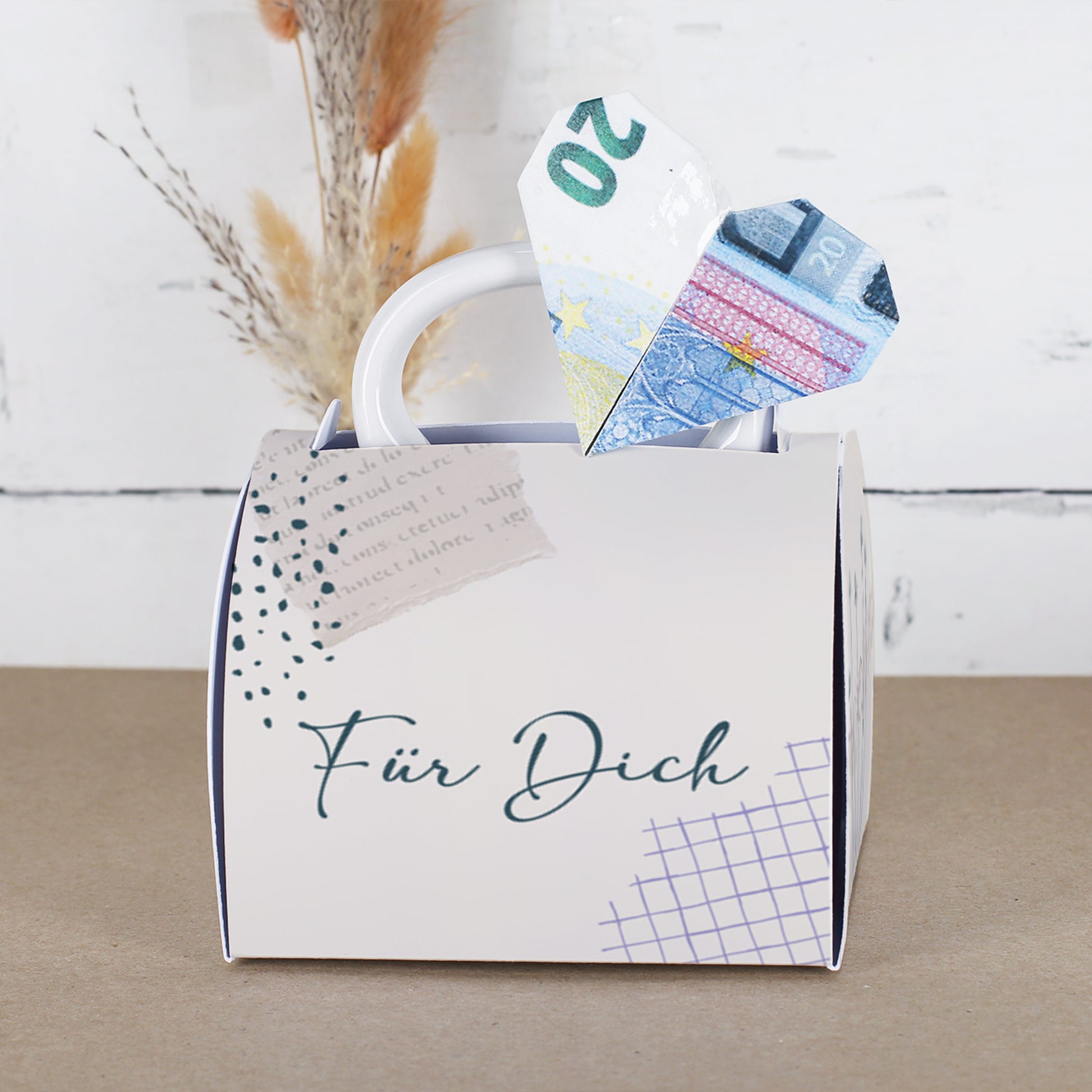 Fototasse in Geschenkverpackung mit „Für Dich“-Aufschrift, aus der ein Herz aus einem gefalteten 20-Euro-Schein ragt. Die Verpackung hat ein dezentes, modernes Design mit grafischen Elementen und wirkt wie eine kleine Handtasche.