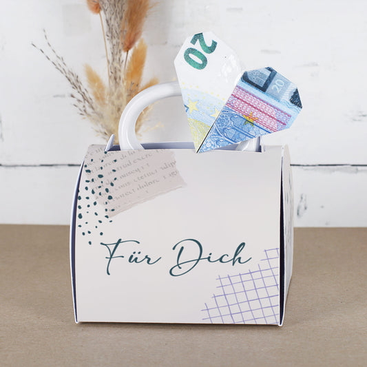 Fototasse in Geschenkverpackung mit „Für Dich“-Aufschrift, aus der ein Herz aus einem gefalteten 20-Euro-Schein ragt. Die Verpackung hat ein dezentes, modernes Design mit grafischen Elementen und wirkt wie eine kleine Handtasche.