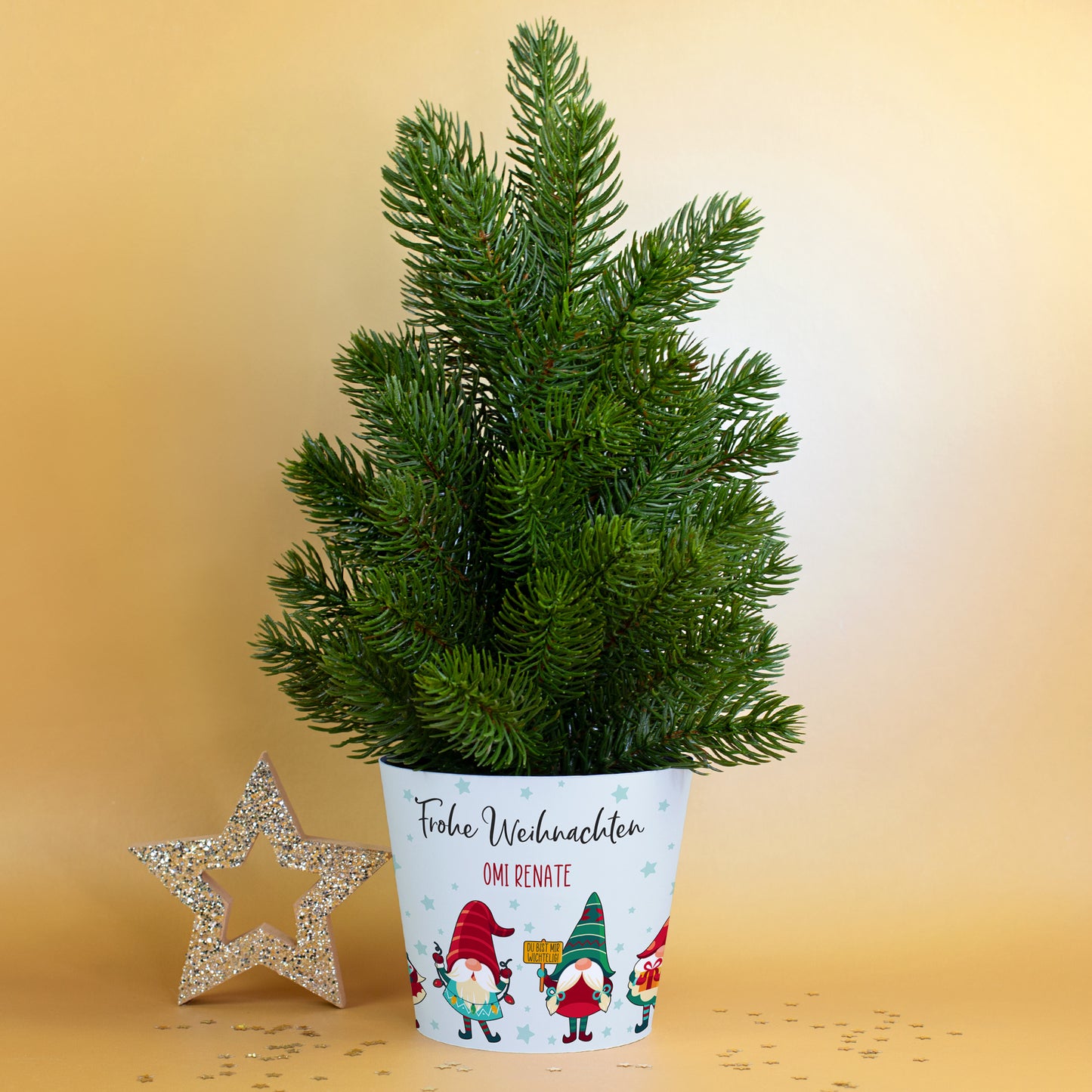 Künstlicher Mini-Weihnachtsbaum mit Wichtel-Banderole und Stern-Deko vor goldenem Hintergrund