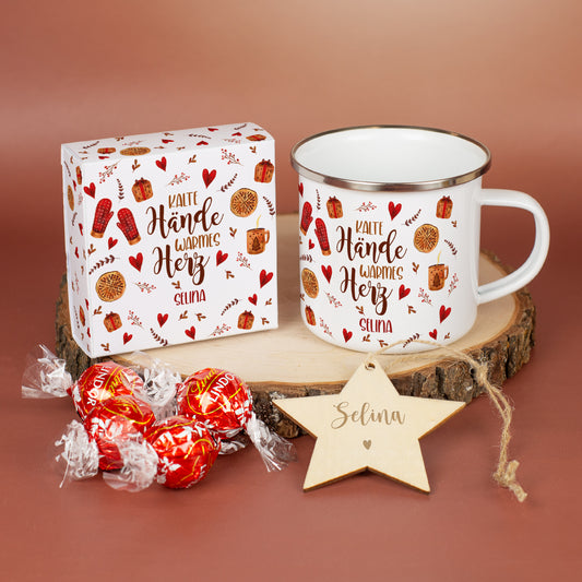 Nahaufnahme des Inneninhalts: Personalisierte Metalltasse mit Spruch „Kalte Hände warmes Herz“ und Name „Selina“. Daneben die dazugehörige Geschenkbox mit vier Lindorkugeln im gleichen Motivdesign sowie ein gravierter Holzstern mit Namensgravur „Selina“, arrangiert auf einer Holzscheibe.