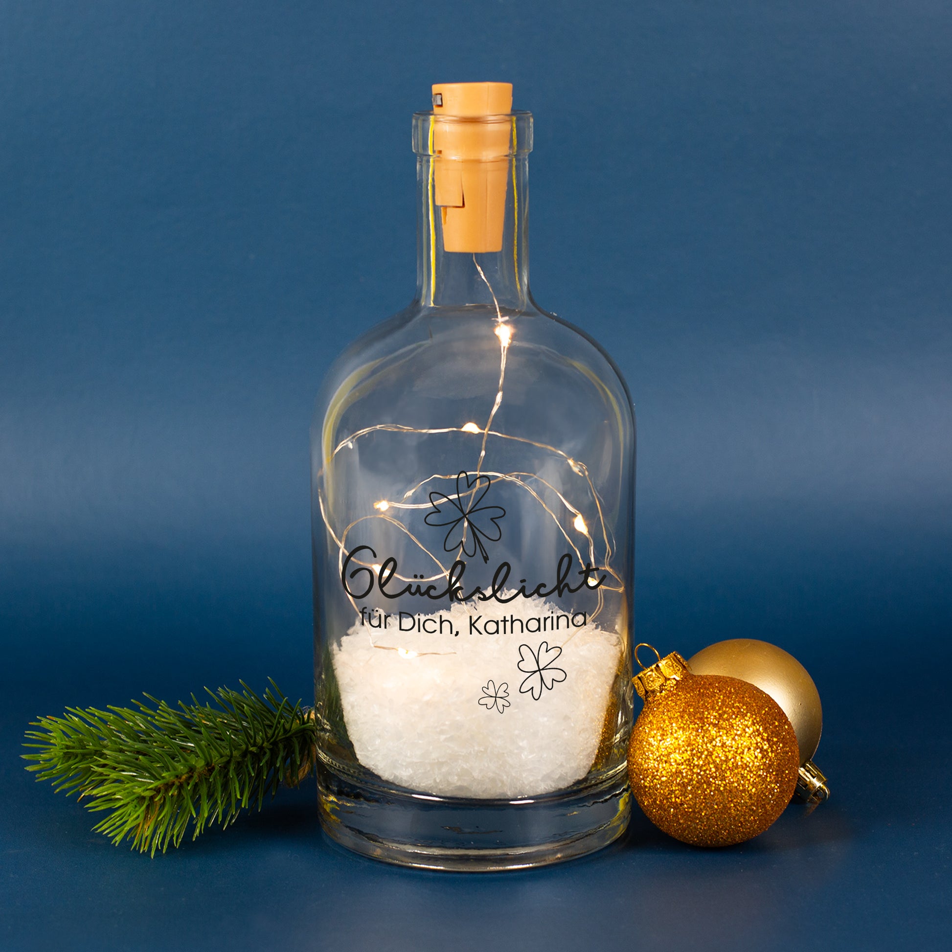 Glückslicht Deko-Karaffe aus Glas mit warmweißer LED-Lichterkette, Kunstschnee und personalisiertem Wunschtext „für Dich, Katharina“, dekoriert mit Tannenzweig und goldenen Weihnachtskugeln.