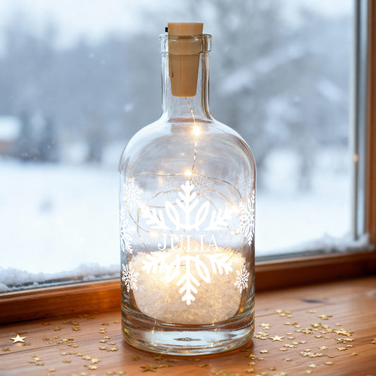Beleuchtete Glasflasche mit Schneeflocken-Design und Name „Julia“ auf Fensterbank im Winter.