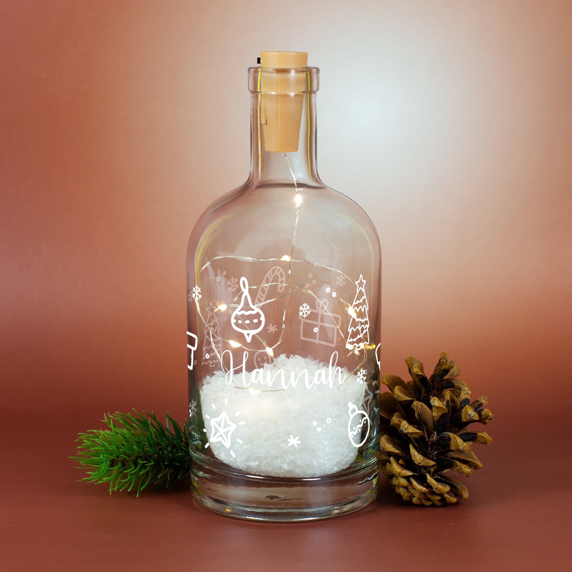 Weihnachtliche LED-Schneekaraffe mit Ornamentdruck, personalisiertem Namen „Hannah“, Kunstschnee und Tannenzweig-Deko mit Zapfen.