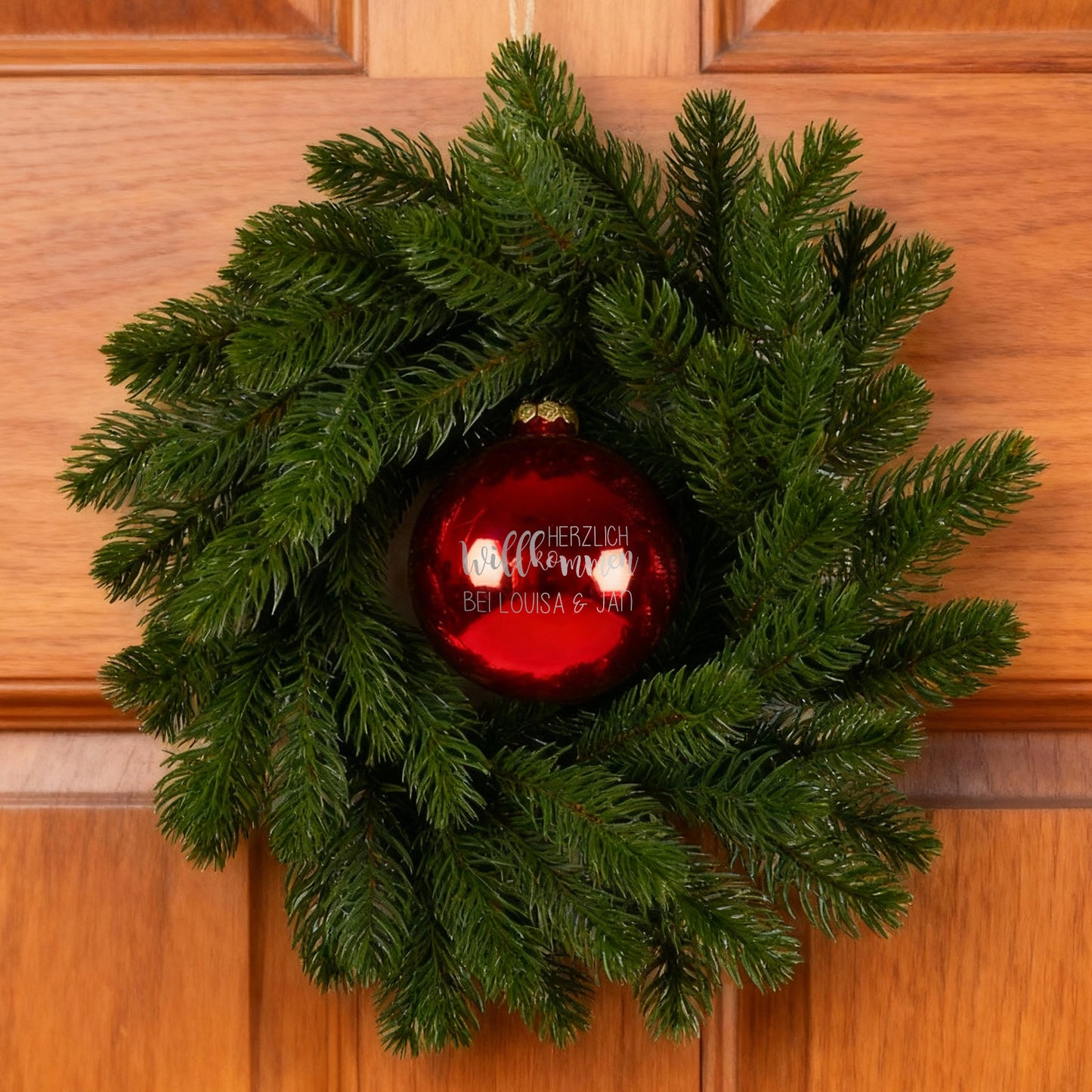 Türkranz mit roter persönlicher Weihnachtskugel an Holzhaustür