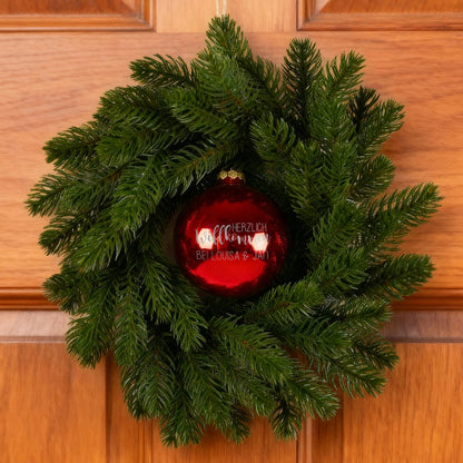 Türkranz mit roter persönlicher Weihnachtskugel an Holzhaustür