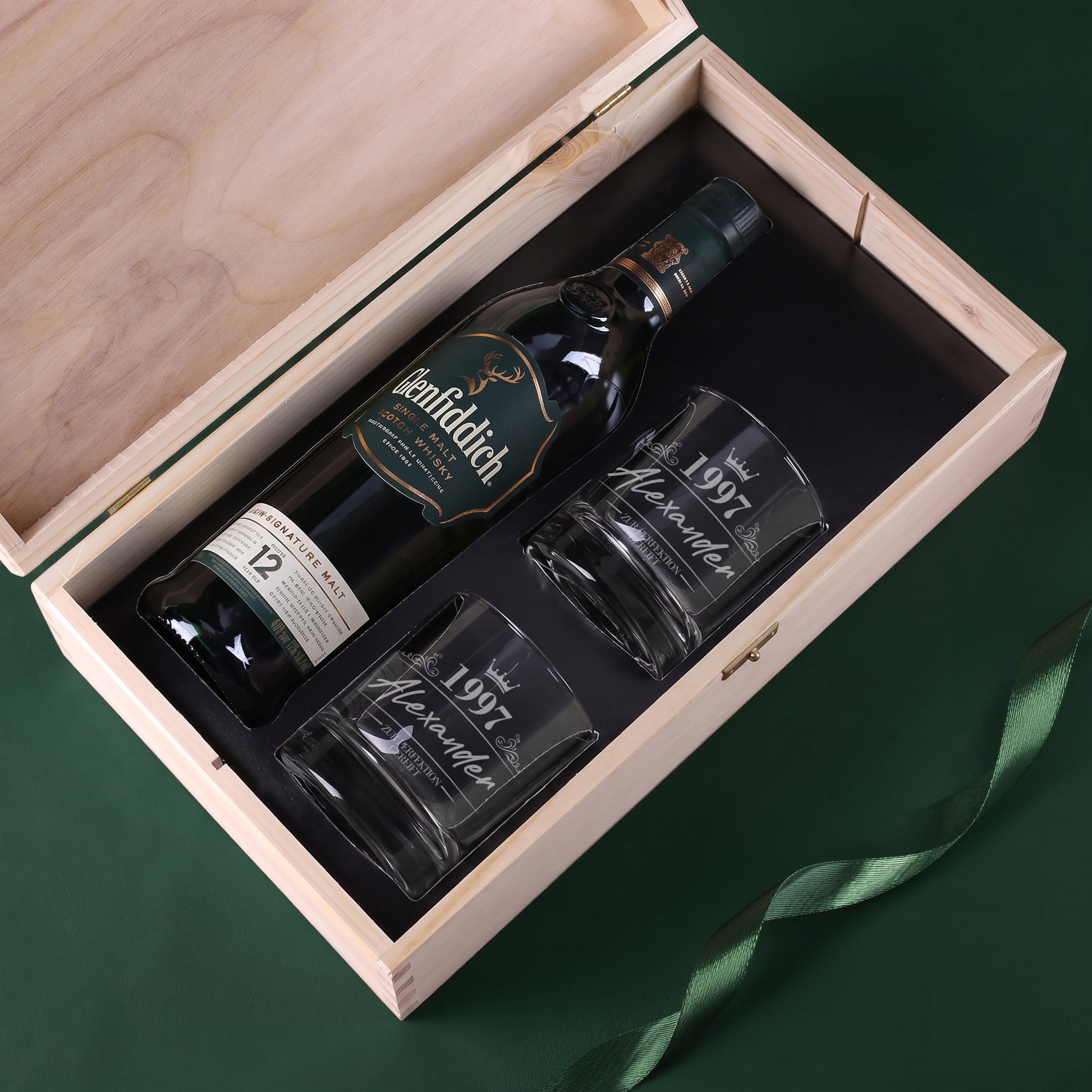 Offene Holzkiste mit Glenfiddich Whiskyflasche und zwei gravierten Whiskygläsern im schwarzen Inlay