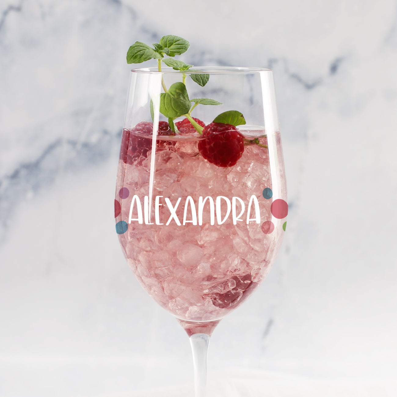 Personalisiertes Weinglas mit bunten Punkten und Name „Alexandra“, gefüllt mit rosa Getränk, Eis, Himbeere und Minze