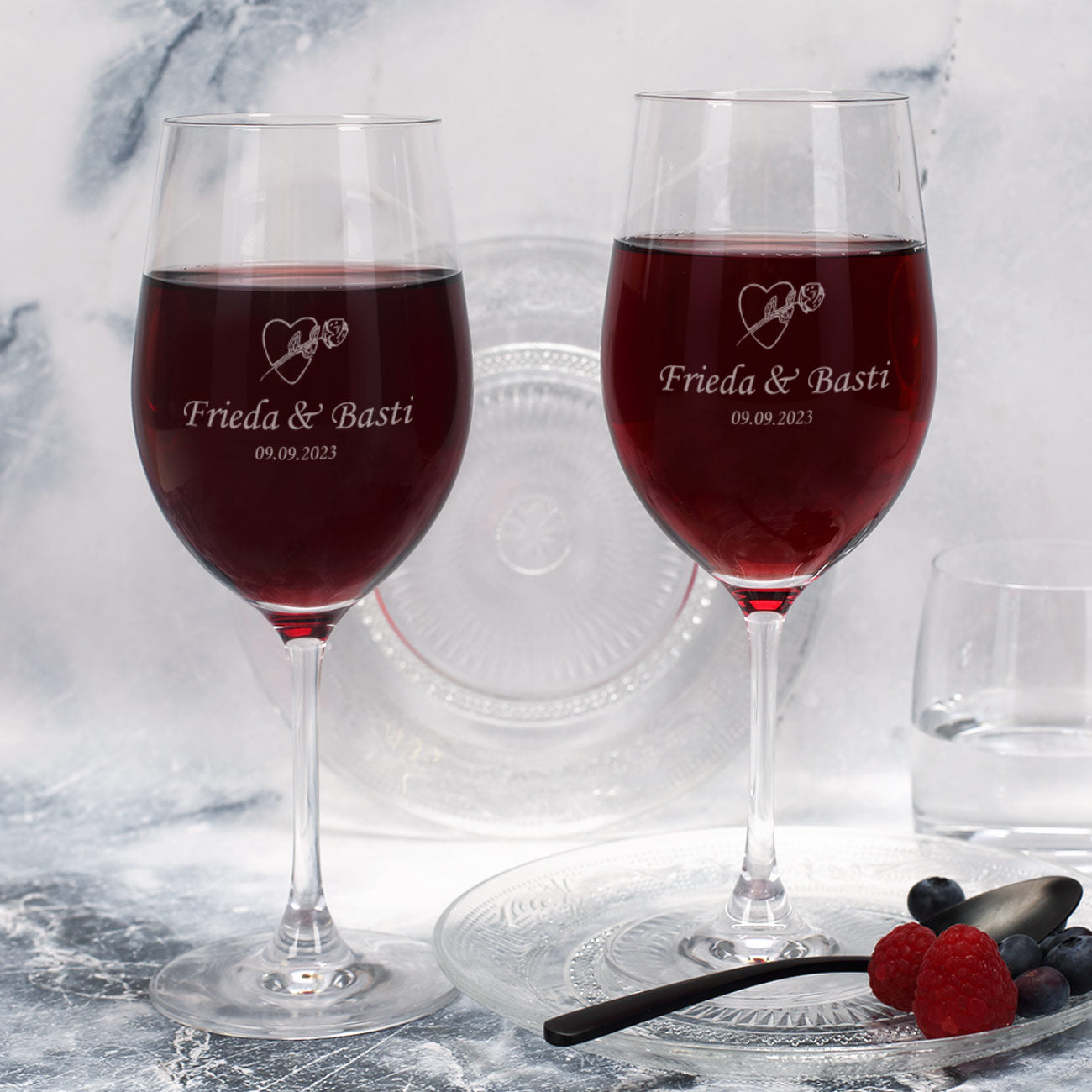 Detailaufnahme zweier Weingläser mit Gravur „Frieda & Basti – 09.09.2023“ und Herz-Rosen-Motiv
