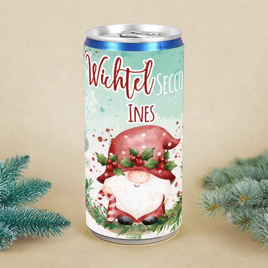 Personalisierte Secco-Dose mit Wichtelmotiv, roter Mütze, Mistelkranz und Name Ines, dekoriert mit Tannenzweigen als Weihnachtsgeschenk.