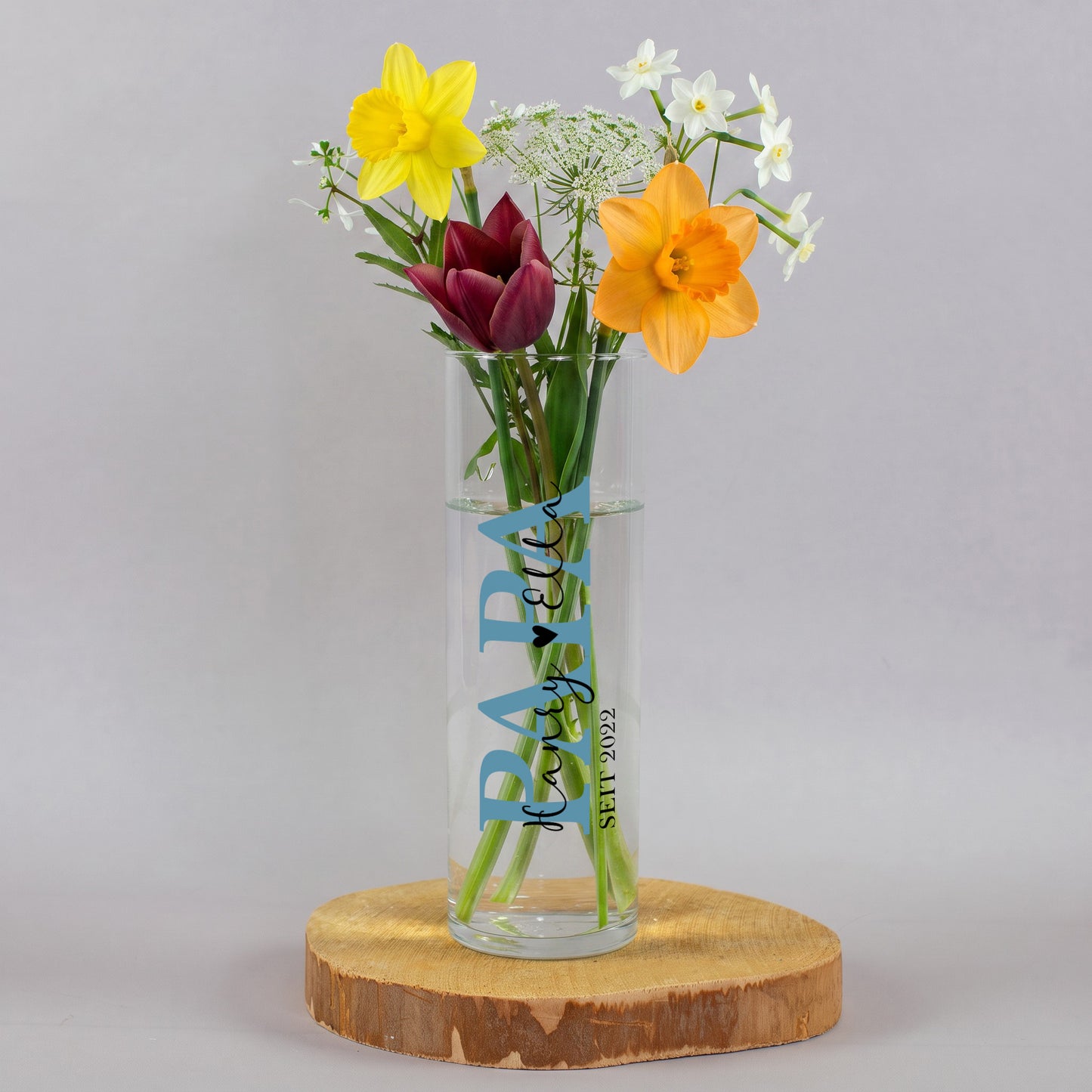 Schmale Glasvase für Papa mit Wunschtext, Herzsymbol und Jahreszahl 2010, gefüllt mit bunten Blumen und als dekoratives Geschenk arrangiert