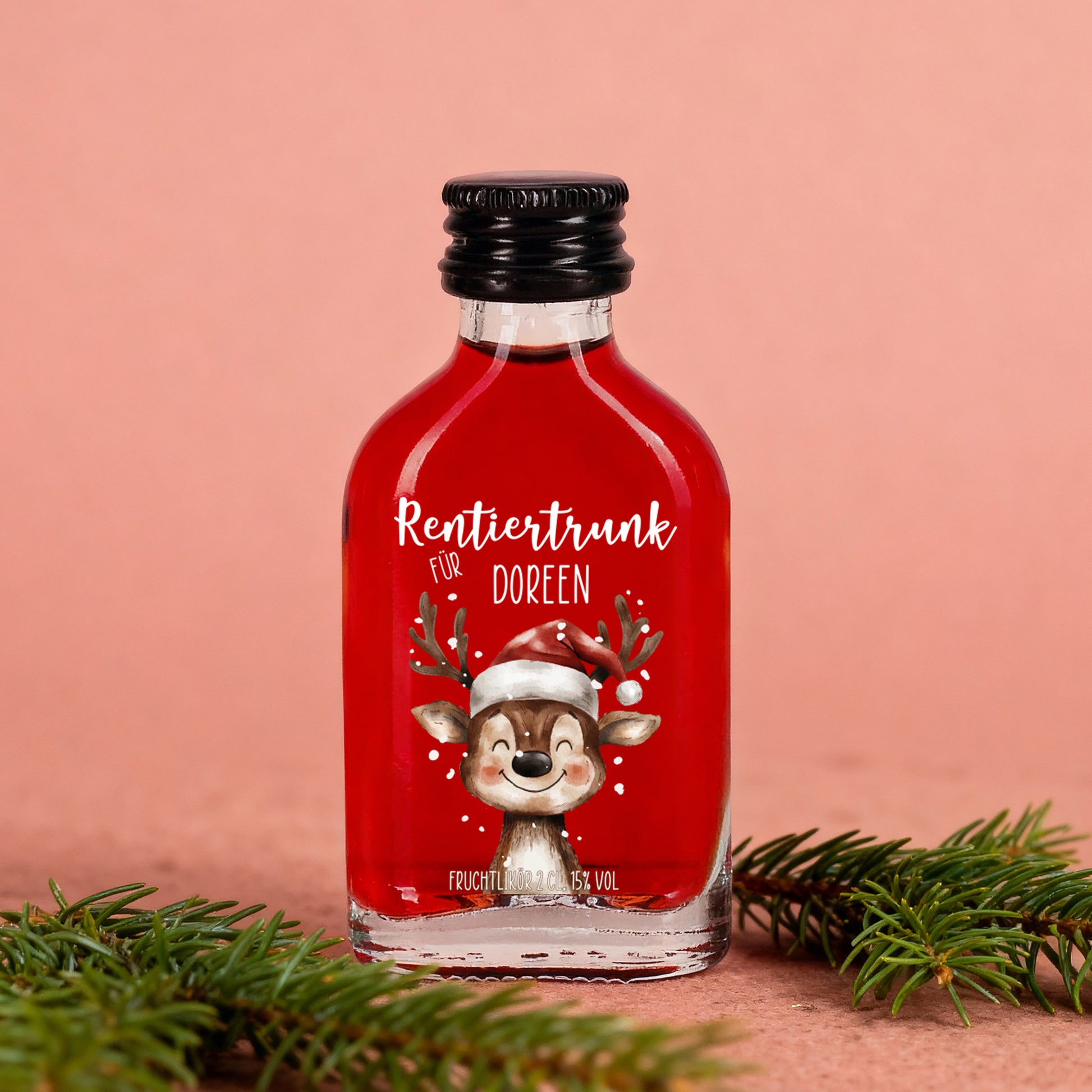 Fruchtlikör-Flasche „Rentiertrunk für Doreen“ auf rosafarbenem Hintergrund mit Tannengrün, winterliche Szene mit rotem Likör und liebevollem Etikett.