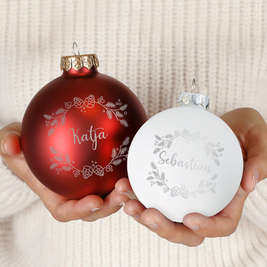 Zwei Weihnachtskugeln – Rot und Weiß – in matter und glänzender Ausführung mit Gravur „Katja“ und „Sebastian“, festlich dekoriert auf Tannenzweigen.