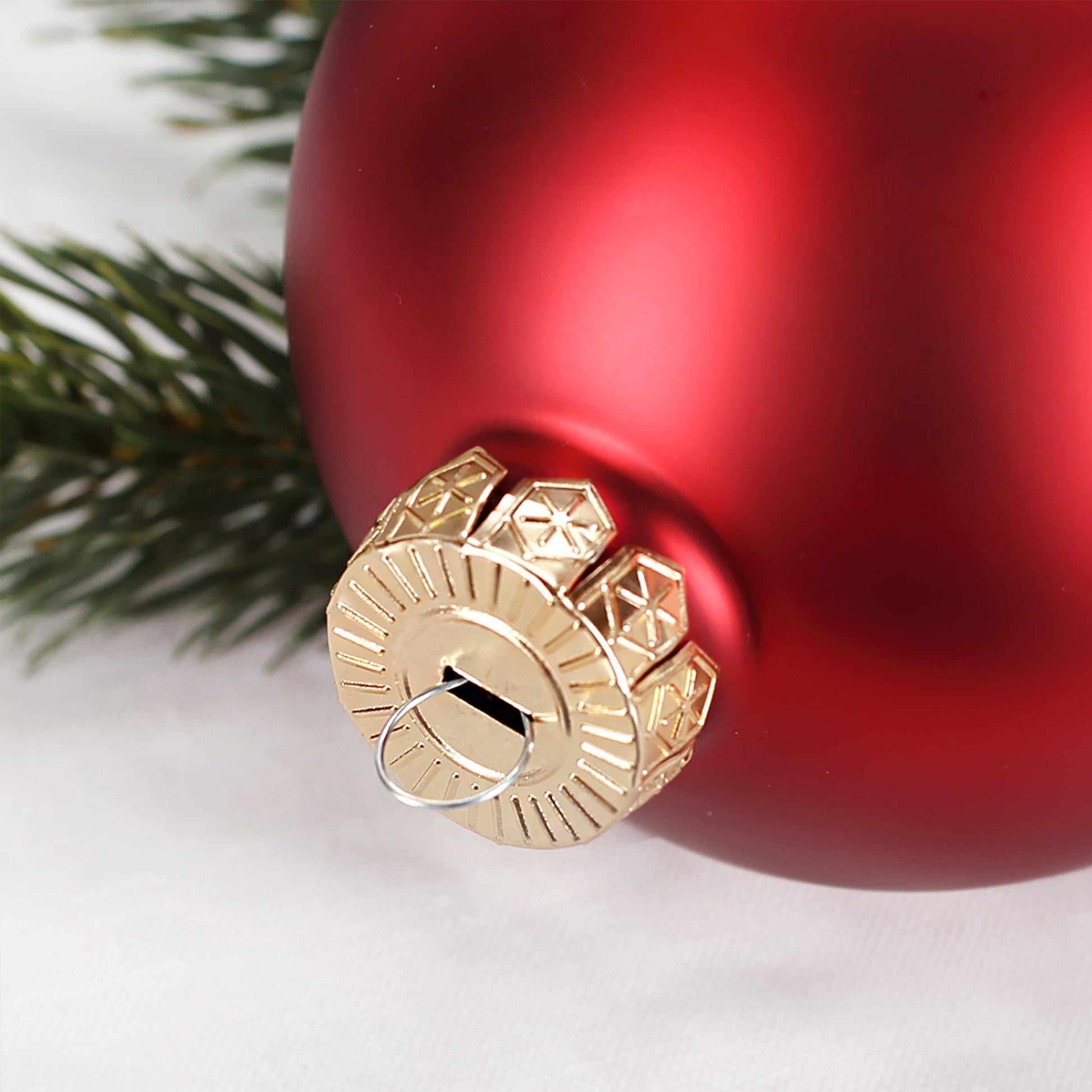 Detailaufnahme der goldfarbenen Aufhängung einer roten Weihnachtskugel mit fein graviertem Kranz und Namensgravur.