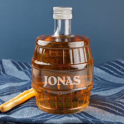 Gravierte Whisky-Flasche in Fassform mit Name JONAS, dekoriert mit Salzstange, auf blauem Tuch