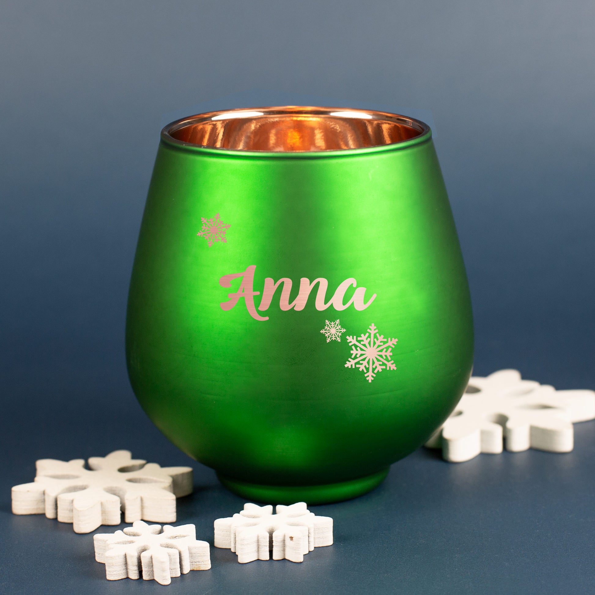 Grünes Windlicht mit Gravur und Schneeflockenmotiv, weihnachtlich dekoriert mit Holzsternen auf dunklem Hintergrund.