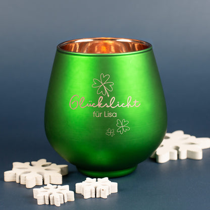 Grünes Windlicht mit Gravur „Glückslicht für Lisa“ und Kleeblättern, umgeben von weißen Deko-Schneeflocken