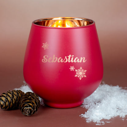 Rotes Windlicht mit Gravur „Sebastian“ und Schneeflockenmotiv, auf braunem Untergrund mit Kiefernzapfen und Kunstschnee dekoriert.